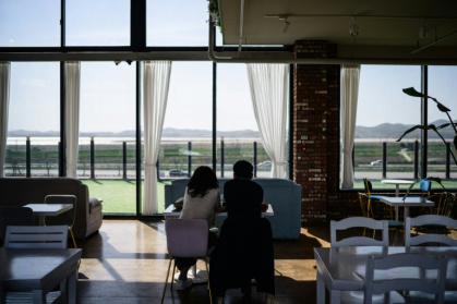 Reclining on sofas at a South Korean cafe, customers sip iced americanos as they gaze past barbed wire fences and watchtowers at the mountains of North Korea - ANTHONY WALLACE